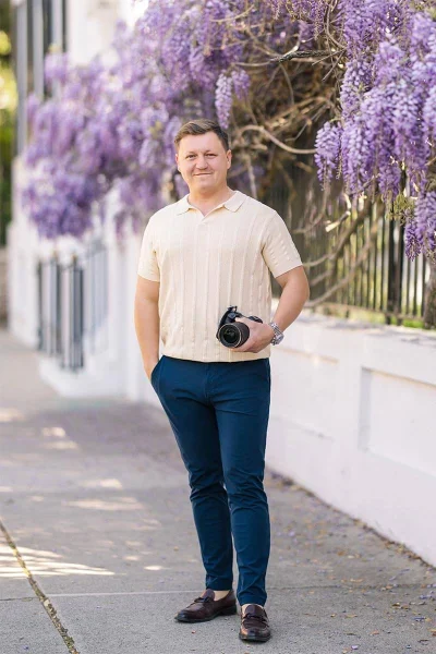 Dennis, lead photographer at Charleston Photo Art, holding his camera on a Charleston street beneath flowering wisteria